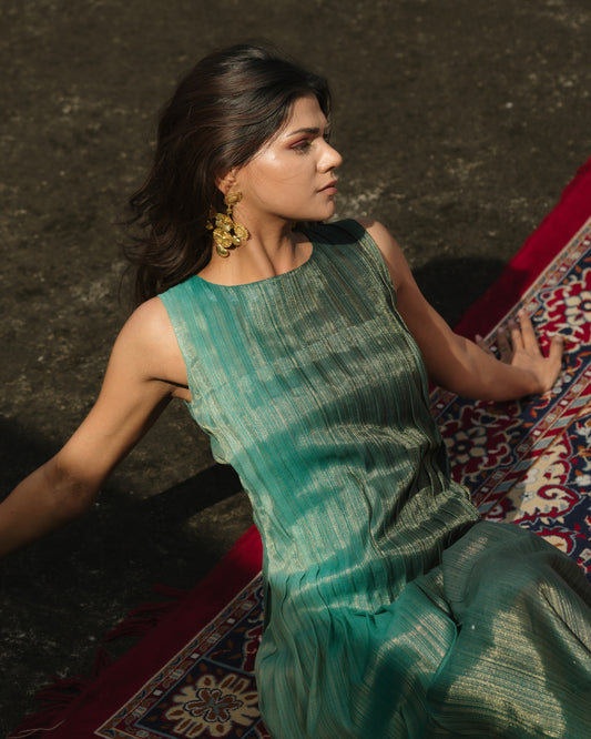 Model wearing teal pleated silk dress from Erised’s Gold Line Collection, featuring handwoven texture and sculptural pleats.