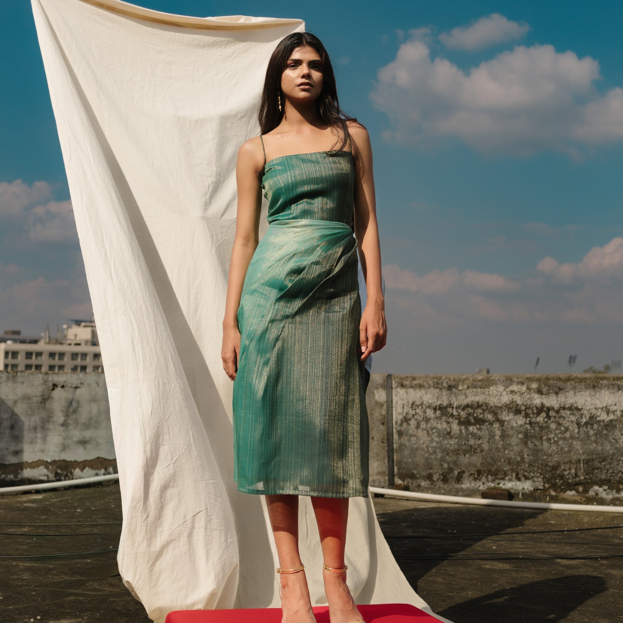 Model wearing teal handwoven bias-draped silk dress with spaghetti straps from Erised’s Gold Line Collection — modern festive luxury look.