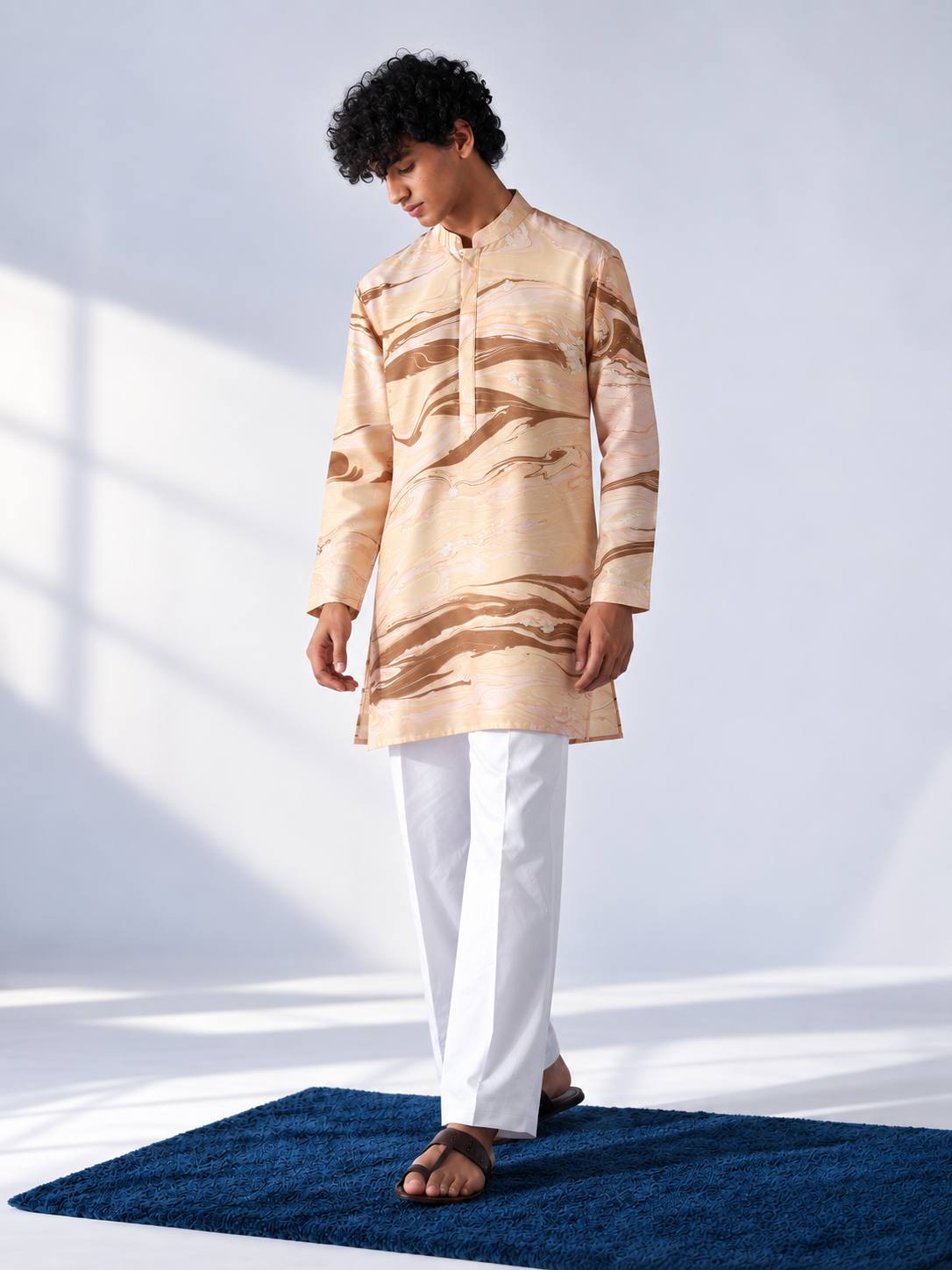  Model wearing a champagne and caramel hand-marbled thigh-length kurta with full sleeves, a band collar and white trousers.