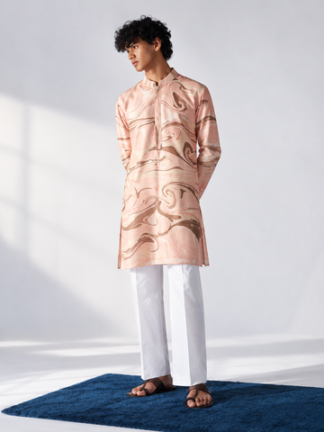 Model wearing a peach thigh-length kurta with all-over brown and ivory hand marbling, full sleeves and white trousers.