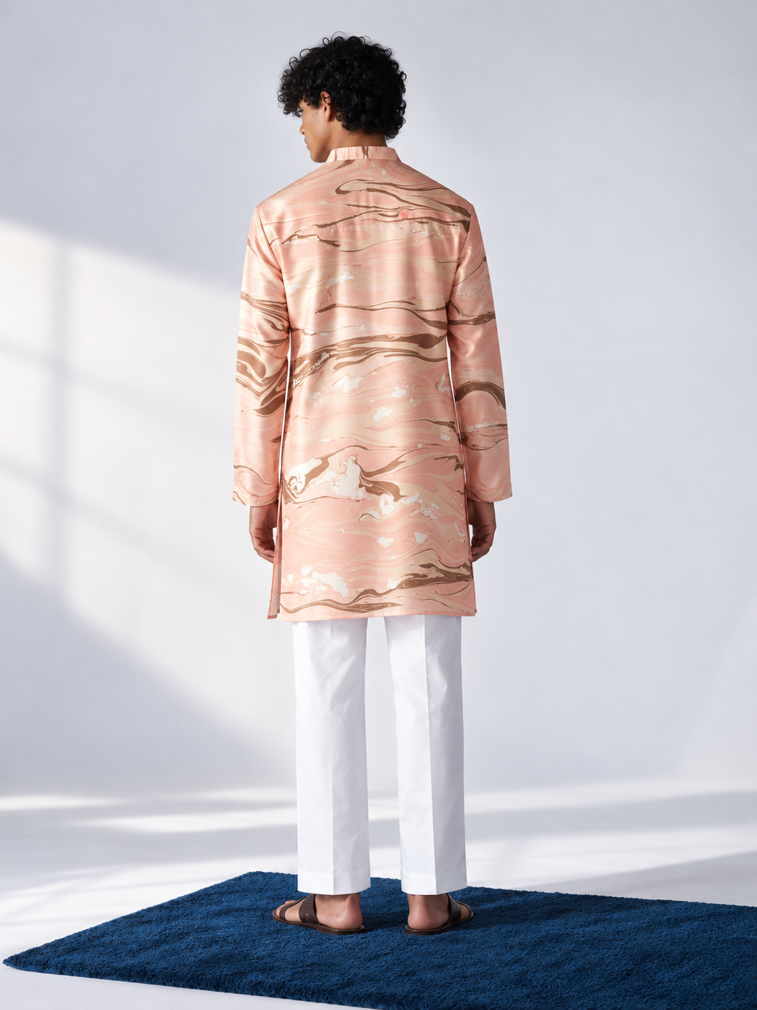 Model wearing a peach thigh-length kurta with all-over brown and ivory hand marbling, full sleeves and white trousers.