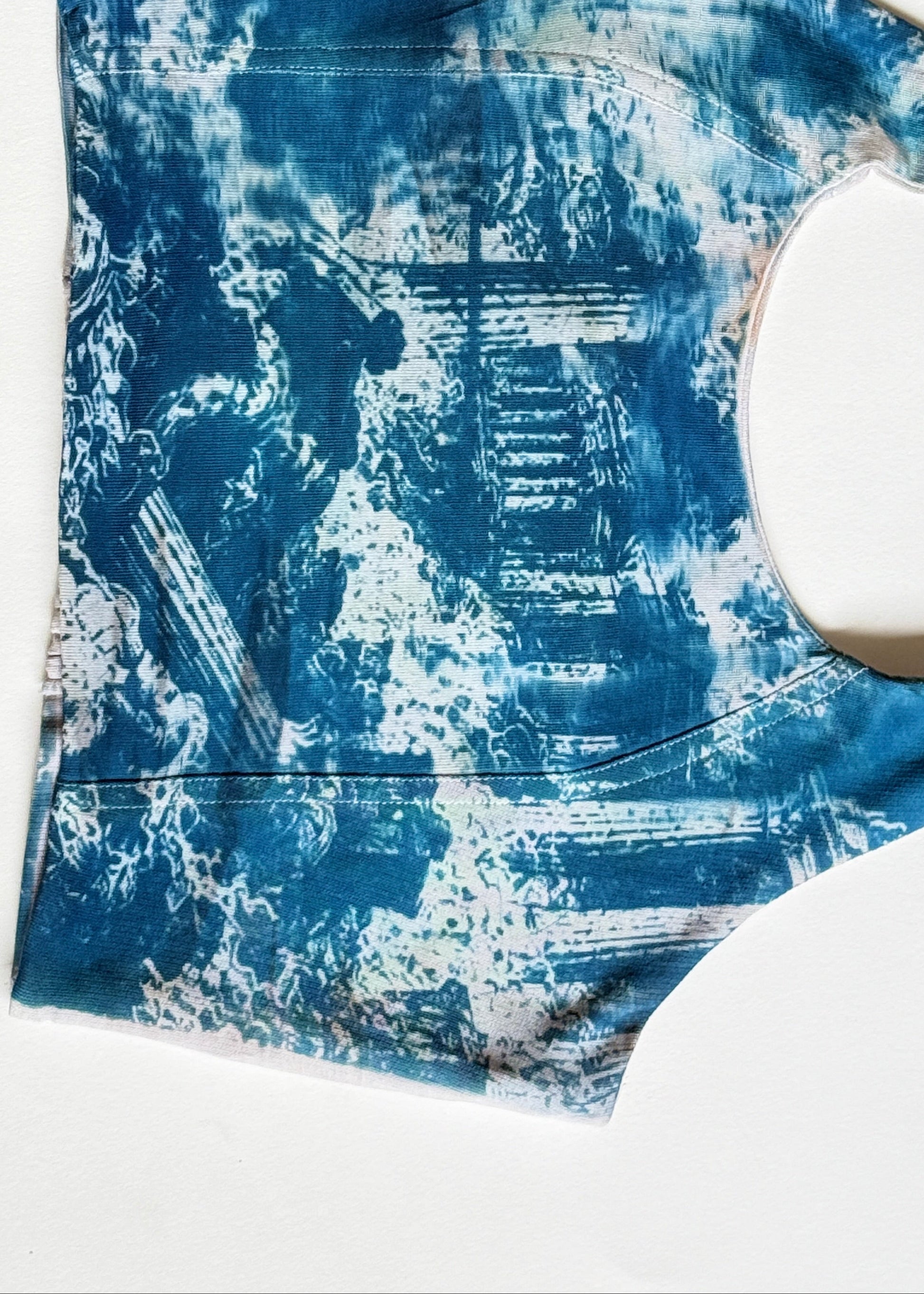 A sleeveless tank top with a blue and white indigo-style tie-dye pattern, laid flat on a white background.